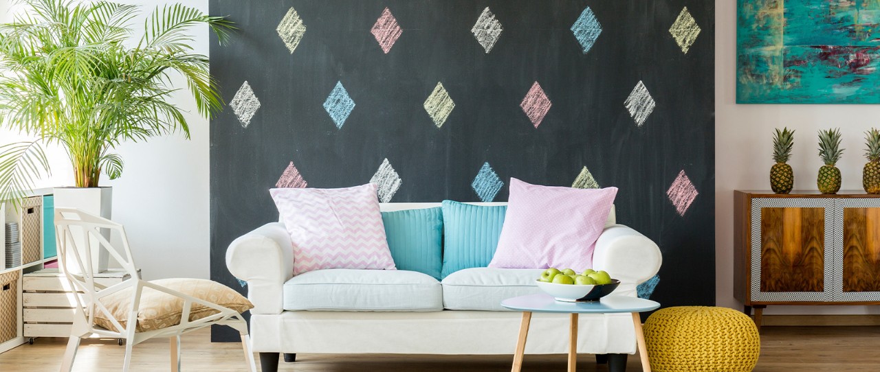 Living room with small sofa featuring colorful accent pillows set in front of a black chalkboard wall with matching colored diamond pattern.